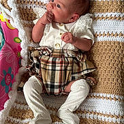 Bella-Rose is registered to the contest to win money with this photo: baby, infant, blanket, crocheted_blanket, plaid_skirt, white_outfit, sitting, hand_in_mouth, cute, newborn, indoors, patterned_blanket, soft_texture, child, portrait, resting, small_person, furniture, home, colorful_background