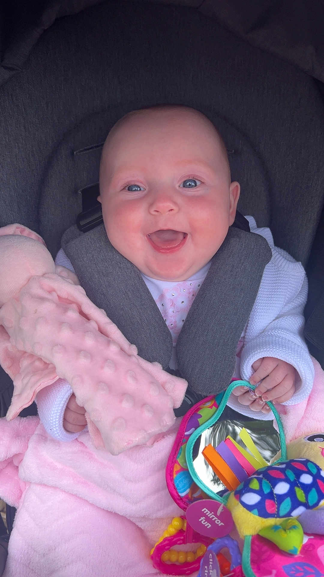 Hallie is registered to the contest to win money with this photo: baby, smiling, car_seat, toy, mirror, plush_toy, pink_blanket, white_clothing, happy, child, infant, seatbelt, colorful, hand, face, closeup, indoors, cute, soft_texture, joy