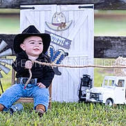 Jacob joined the competition — help win amazing prizes! black_shirt, boots, chair, child, cowboy, decor, fence, grass, hat, jeans, lantern, outdoor, playful, portrait, rope, rustic, smiling, toy_truck, windmill, young_child