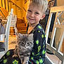 child, kitten, cat, indoor, smile, pajamas, star_pattern, chair, stairs, furniture, happy, pet, gray_cat, young_child, portrait, cozy, home, cute, animal, person