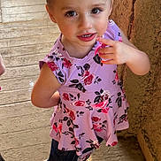 Lilianna is registered to the contest to win money with this photo: child, girl, floral_top, denim_shorts, sandal, wooden_floor, wall, finger_on_mouth, curious_expression, natural_light, indoors, standing, brown_hair, big_eyes, summer_clothing, casual, cute, young, portrait, person