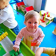 Wendy a rejoint le concours — aidez-le/la à gagner de superbes lots ! toddler, child, playing, building_blocks, toy, indoor, table, colorful, pink_shirt, blonde_hair, kids, playroom, window, daylight, happy, smiling, person, curly_hair, plastic_blocks, wooden_toy