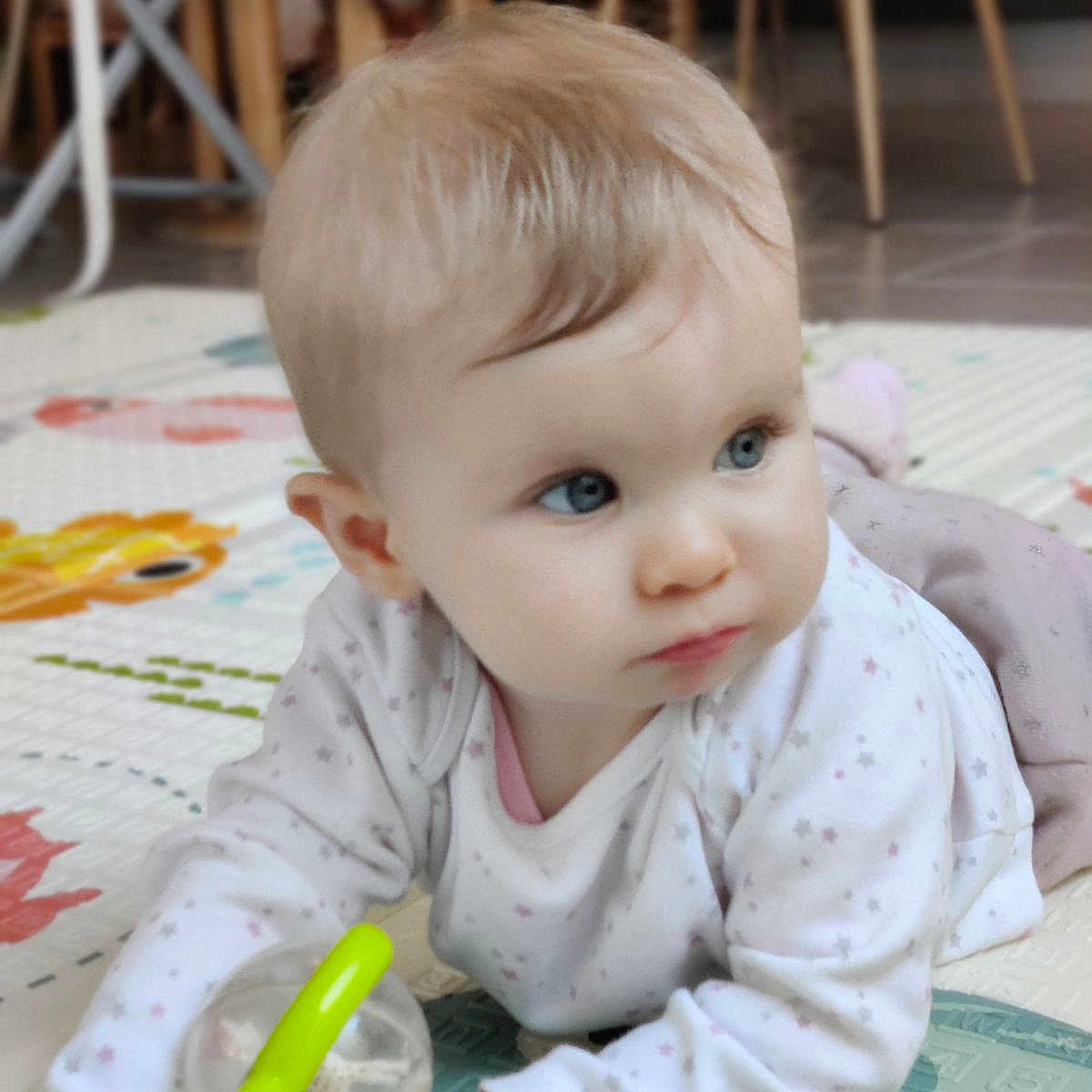 Wendy participe au concours pour gagner de l'argent avec cette photo : baby, blue_eyes, blurred_background, child, clothing, crawling, curious, face, floor, furniture, hand, indoor, infant, light_hair, long_sleeve, person, play_mat, rattle, toy, wooden_chair