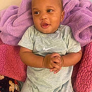 Jeremiah is registered to the contest to win money with this photo: baby, infant, child, blanket, clothing, gray_outfit, nike_logo, hands_clasped, cute, lying_down, indoor, soft_texture, colorful_blankets, happy_expression, portrait, young, sleepwear, plush, skin, face