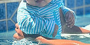 Ezekiel is registered to the contest to win money with this photo: baby, child, water, pool, swimming_pool, hat, striped_clothing, sun_hat, blue, white, hands, reflection, outdoor, summer, infant, cute, person, skin, water_surface, holding