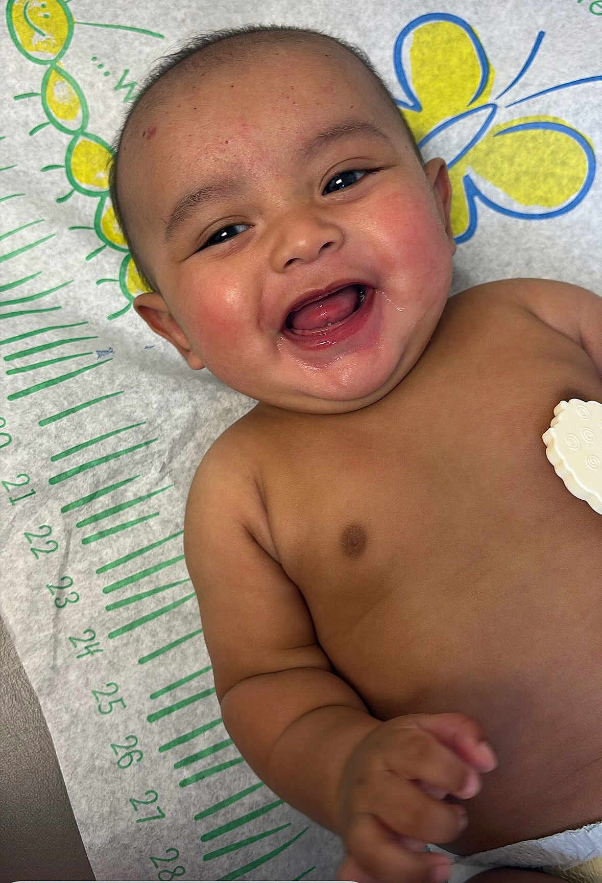 Ezekiel is registered to the contest to win money with this photo: baby, smiling, happy, infant, child, face, skin, mouth, eyes, hand, lying_down, background_pattern, colorful, cute, portrait, cheerful, indoors, closeup, expression, young