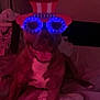 animal, bed, blanket, blue_light, brown, canine, costume, dog, funny, furniture, glasses, hat, indoor, novelty_glasses, pet, red_hat, relaxed, smiling, tongue_out, white_chest