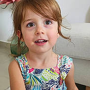 Lyvia participe au concours pour gagner de l'argent avec cette photo : big_eyes, brown_hair, carpet, casual, child, colorful_dress, cute, earrings, flower, girl, happy, home, indoor, person, portrait, sitting, smiling, sofa, toddler, young