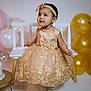 Layla is registered to the contest to win money with this photo: baby, balloons, bench, bow, cake_table, celebration, child, dress, earrings, formal_dress, gold, headband, indoor, lace, party, portrait, shoes, smile, studio, toddler