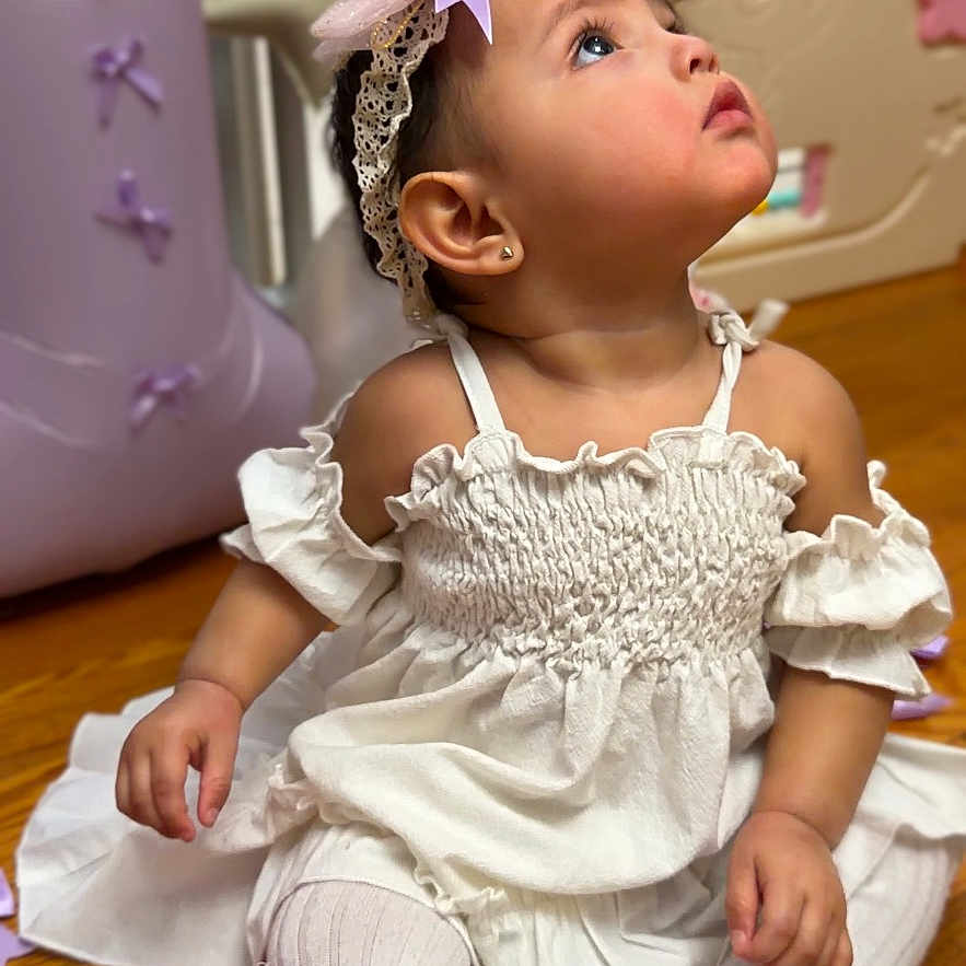 Layla joined the competition — help win amazing prizes! accessory, baby, child, closeup, curious, cute, decorations, fashion, girl, headband, indoors, playful, portrait, purple_bow, sitting, soft_lighting, tights, white_dress, wooden_floor, young_child