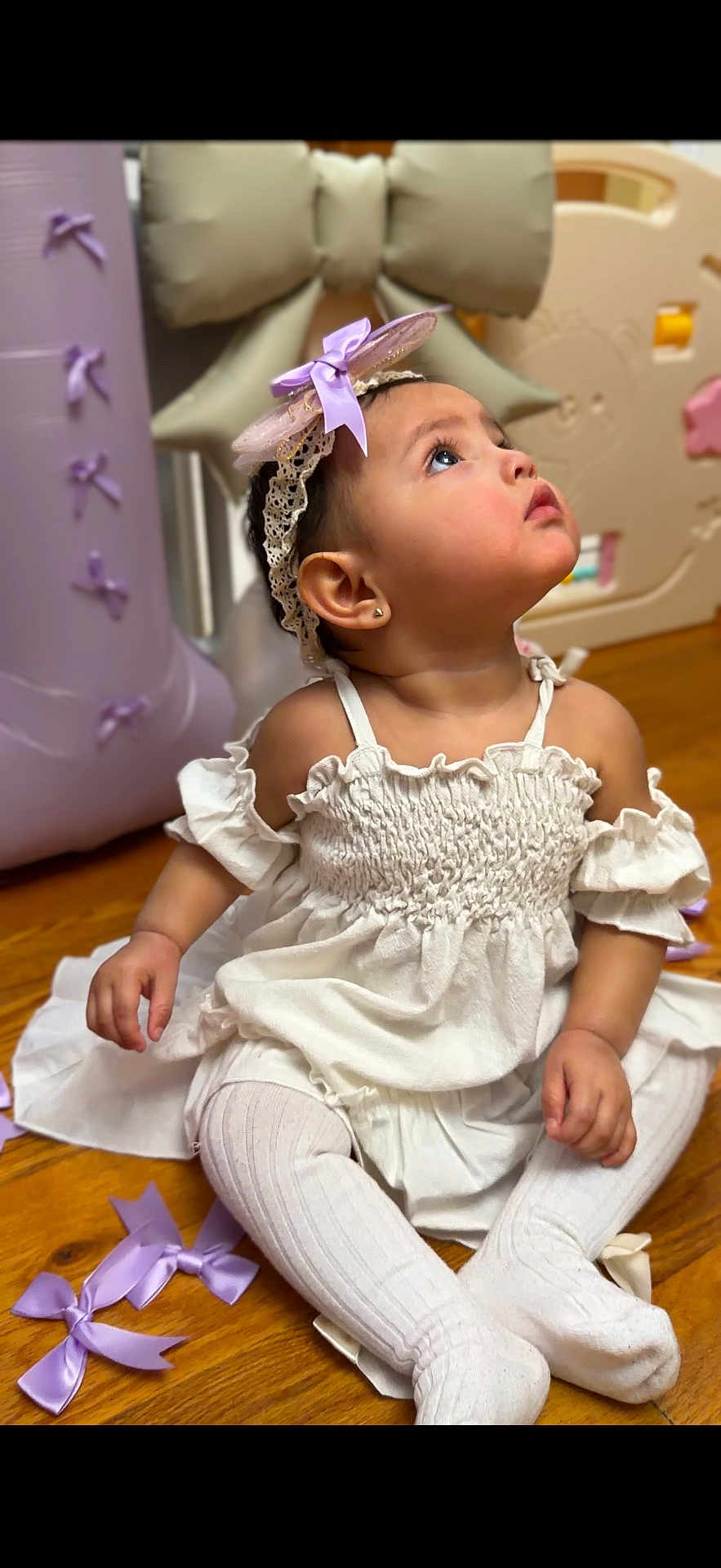Layla joined the competition — help win amazing prizes! baby, child, girl, white_dress, headband, purple_bow, tights, sitting, wooden_floor, curious, indoors, decorations, cute, portrait, young_child, fashion, accessory, playful, soft_lighting, closeup