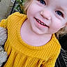 child, toddler, yellow_sweater, smiling, cute, toy, outdoor, plants, garden_center, happy, face, portrait, clothing, person, blue_eyes, young_child, casual, daylight, standing, closeup