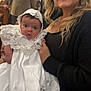 Koda is registered to the contest to win money with this photo: baby, woman, smile, dress, gown, bonnet, lace, indoor, portrait, event, celebration, holding, person, people, face, clothing, happy, ceremony, child, family