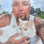 Guero is registered to the contest to win money with this photo: animal, calm, casual, cat, closeup, cloud, daylight, feline, greenery, hand, holding, man, nature, outdoor, person, pet, portrait, sky, tattoo, white_tank_top