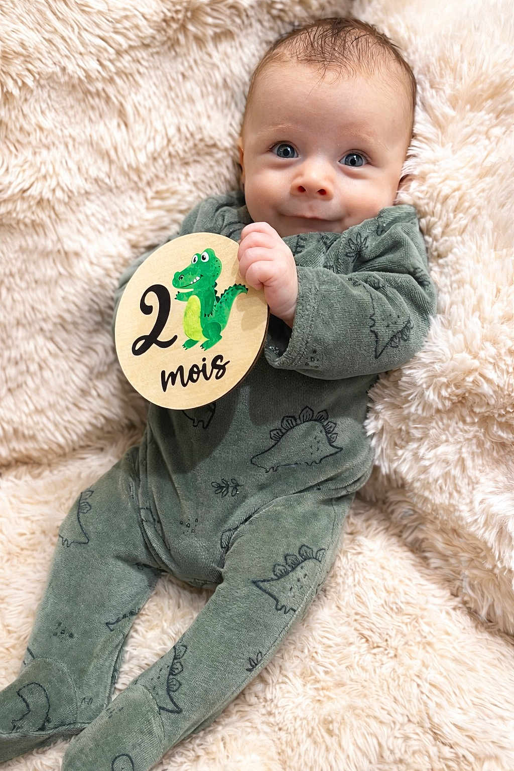 Isaac participe au concours pour gagner de l'argent avec cette photo : baby, infant, child, portrait, blanket, fur_texture, onesie, green_clothing, dinosaur_sign, two_months, month_marker, hand, fingers, big_eyes, smile, cozy, soft_texture, lying_down, closeup, cute