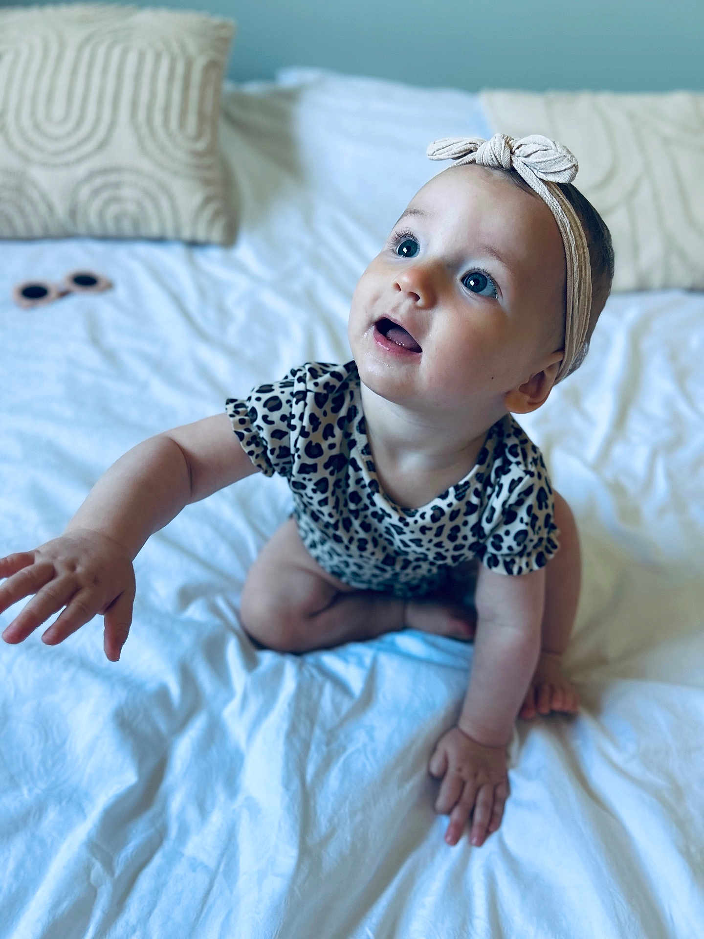 Eléa a rejoint le concours — aidez-le/la à gagner de superbes lots ! baby, bed, blue_eyes, child, closeup, comfortable, crawling, curious, cute, happy, headband, indoors, infant, patterned_clothing, pillows, portrait, reaching_hand, soft_lighting, sunglasses, young_child