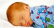 Kassian is registered to the contest to win money with this photo: baby, sleeping, infant, red_hair, onesie, superhero, captain_america, hulk, soft, white_bed, cute, peaceful, portrait, child, face, clothing, resting, newborn, cozy, lying_down