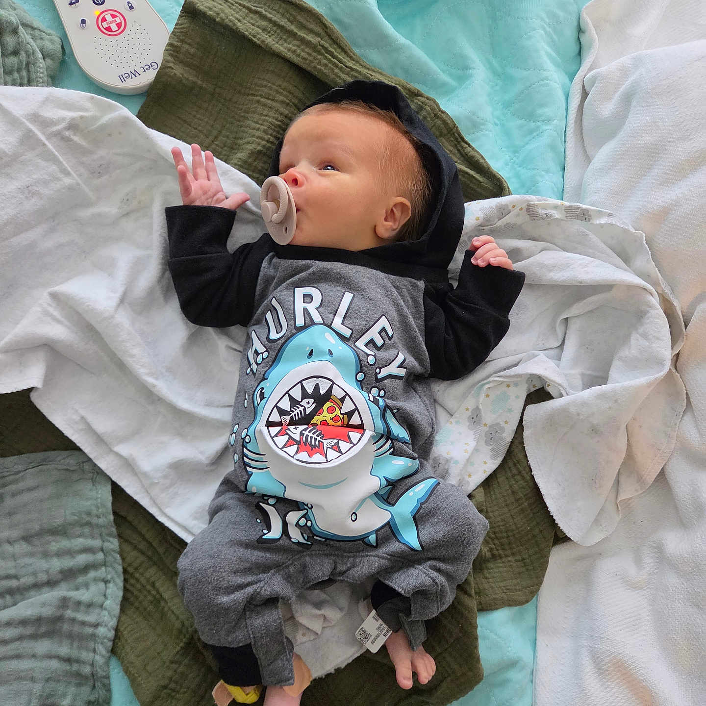 Kassian joined the competition — help win amazing prizes! baby, infant, pacifier, clothing, onesie, shark_design, blanket, quilt, remote_control, bed, sleepwear, foot, hand, lying_down, indoors, comfort, soft_texture, child, cute, resting