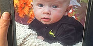 Reggie is registered to the contest to win money with this photo: baby, background_blur, black_jacket, blanket, clothing, cozy, curious, cute, face, flower, framed_photo, hand, indoor, infant, orange_flower, person, photography, portrait, soft_texture, young_child