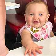 Larry is registered to the contest to win money with this photo: baby, child, infant, smiling, happy, portrait, floral_bib, blue_eyes, seated, high_chair, restaurant, booth, table, snacks, crackers, hand, reaching, indoor, close_up, family
