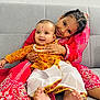 baby, barefoot, celebration, child, couch, cultural, cute, embrace, face_paint, family, happy, indoor, joy, portrait, red_dress, sitting, smiling, toddler, traditional_clothing, yellow_outfit