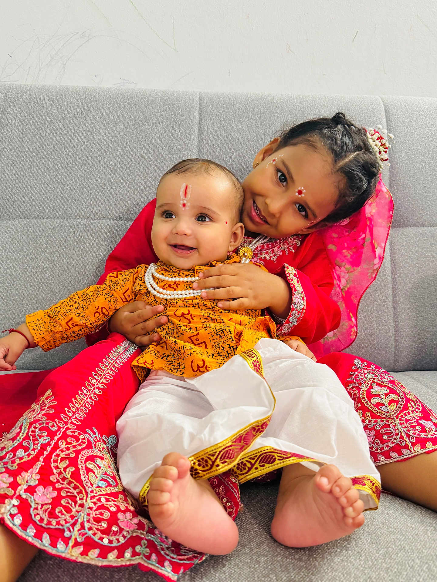 Divit is registered to the contest to win money with this photo: child, baby, smiling, traditional_clothing, red_dress, yellow_outfit, couch, indoor, portrait, happy, face_paint, barefoot, sitting, family, cute, celebration, toddler, cultural, embrace, joy