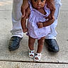toddler, child, adult_hands, white_pants, black_shoes, sidewalk, outdoor, dress, sandals, curly_hair, supporting, standing, concrete, person, baby, cute, small, walking, summer, daylight