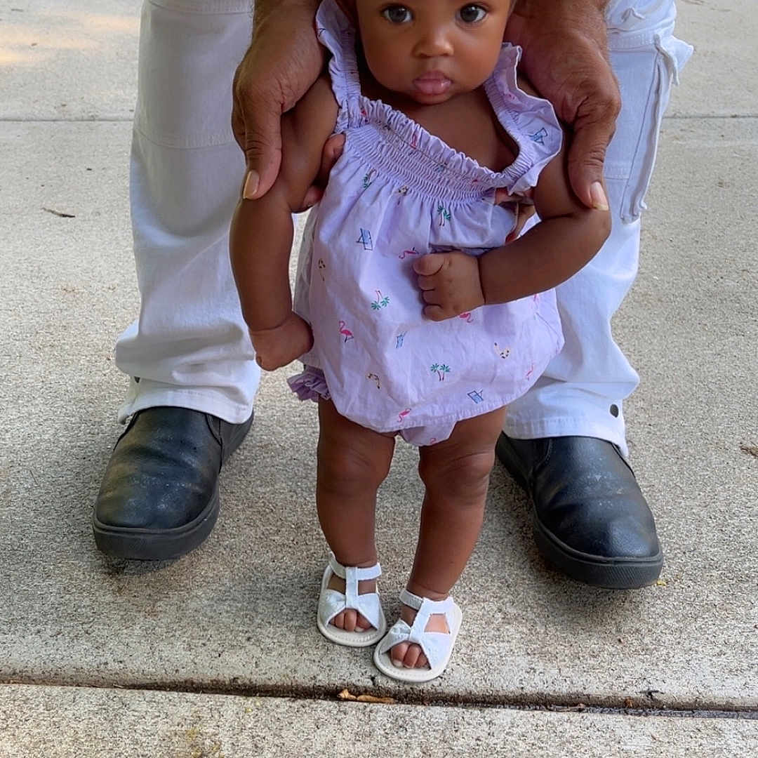 Mackenzie joined the competition — help win amazing prizes! toddler, child, adult_hands, white_pants, black_shoes, sidewalk, outdoor, dress, sandals, curly_hair, supporting, standing, concrete, person, baby, cute, small, walking, summer, daylight