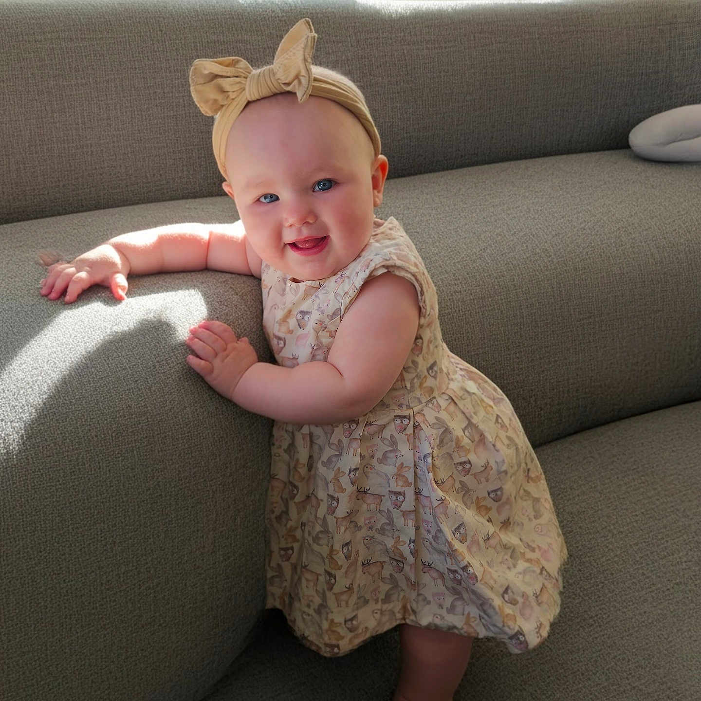 Scarlette joined the competition — help win amazing prizes! baby, barefoot, blue_eyes, bow, child, chubby_cheeks, couch, cute, dress, girl, gray_couch, happy, headband, indoor, infant, natural_light, patterned_dress, portrait, smile, standing