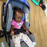 Mickiyah is registered to the contest to win money with this photo: baby, car_seat, infant, pink_shirt, pajamas, baby_bottle, wooden_floor, indoor, child, hair_puffs, clothing, seat_belt, toy, floor, person, baby_gear, casual, cute, relaxed, smiling