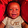 baby, child, clothing, cute, expression, eyes, face, happy, indoors, infant, joy, mouth, onesie, person, portrait, red_background, sitting, skin, smiling, young