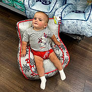 Brayden is registered to the contest to win money with this photo: baby, child, indoor, floor, wood_floor, chair, spiderman, clothing, socks, toy_aisle, store, training_pants, bluey, smirk, casual_pose, red_shorts, grey_tshirt, product_display, baby_chair, shopping