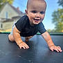 Brayden is registered to the contest to win money with this photo: baby, child, smiling, crawling, trampoline, outdoor, daytime, happy, cute, face, skin, clothing, shorts, black_shirt, nature, trees, house, background, sunlight, portrait