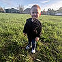 casual_clothing, child, cute, daylight, field, grass, greenery, happy, jacket, nature, outdoor, person, portrait, sky, smile, sneakers, standing, sunlight, toddler, young_child