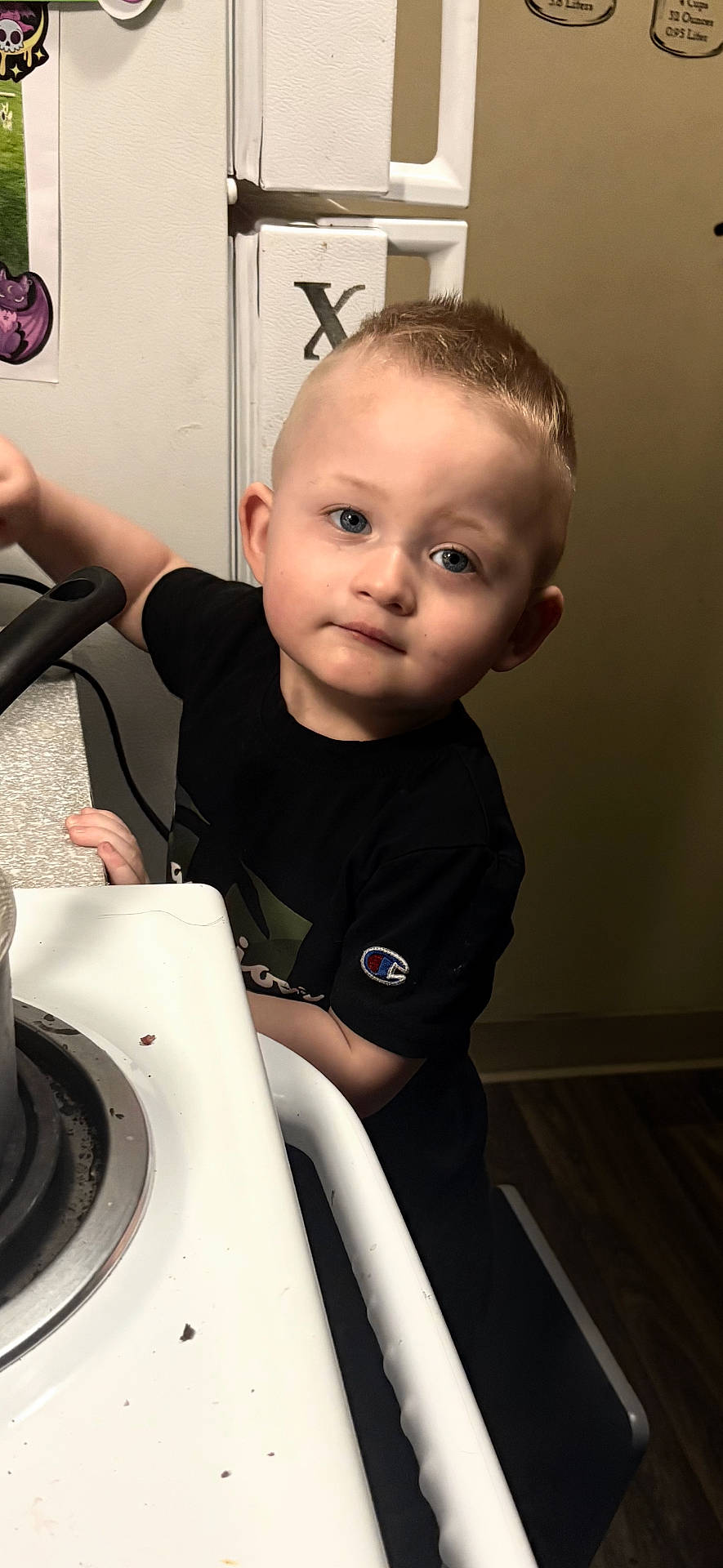 appliance, baby, bodypart, clothing, device, electricaldevice, face, finger, hand, handrail, head, indoors, kitchen, oven, person, photography, portrait, stove, t_shirt, wood