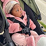 baby, child, stroller, pink_clothing, hat, booties, jacket, straps, outdoor, curious, face, person, seat, infant, cute, warm_clothing, side_profile, black_hair, bundle, transportation