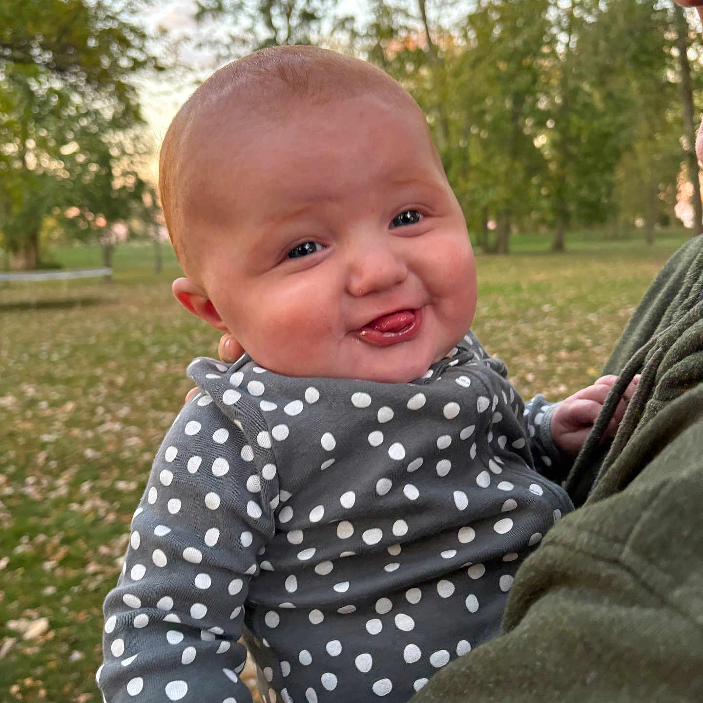 Quinn is registered to the contest to win money with this photo: baby, clothing, face, grass, happy, head, knitwear, laughing, nature, outdoors, park, pattern, person, photography, plant, portrait, smile, sweater, tree, vegetation