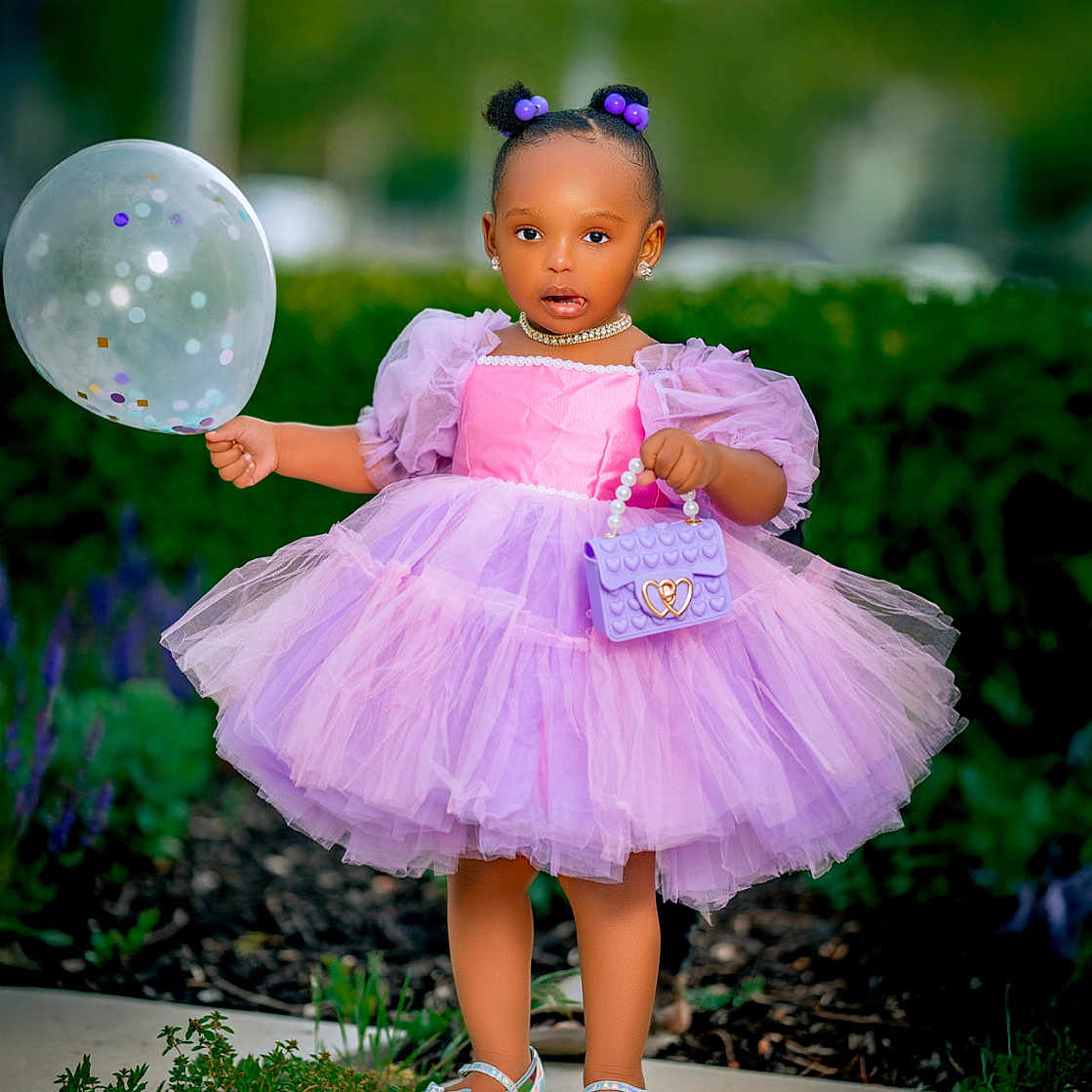 Mlonge is registered to the contest to win money with this photo: accessories, balloon, child, cute, earrings, fashion, garden, greenery, hair_buns, happy, necklace, outdoor, pathway, portrait, purple_dress, purse, shoes, standing, toddler, tutu