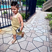 Bryton is registered to the contest to win money with this photo: child, boy, toy_car, walking, sidewalk, fence, pool, outdoor, summer, shorts, sandals, haircut, play, daylight, pavement, greenery, recreation, casual_clothing, happy, sunny