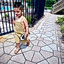 child, boy, toy_car, walking, sidewalk, fence, pool, outdoor, summer, shorts, sandals, haircut, play, daylight, pavement, greenery, recreation, casual_clothing, happy, sunny