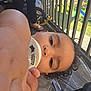 Meilani is registered to the contest to win money with this photo: toddler, child, baby_bottle, curly_hair, hand, face, person, balcony, railing, footwear, sandals, outdoor, daylight, plastic_cover, toy_wheel, grass, leg, shirt, skin, close_up
