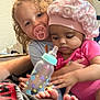 Amira joined the competition — help win amazing prizes! baby, baby_bottle, bottle, child, closeup, curly_hair, cute, expression, face, family, foot, hand, hat, holding, indoor, pacifier, person, pink_clothing, sitting, toddler