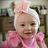 baby, baby_girl, background_blur, child, closeup, cute, face, flower, furniture, happy, headband, home_interior, indoor, infant, person, pink_clothing, portrait, smile, soft_lighting, young_child