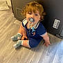 Jax joined the competition — help win amazing prizes! baby, child, pacifier, curly_hair, blue_eyes, socks, romper, floor, wooden_floor, indoor, appliance, home, sitting, cute, infant, young_child, looking_up, clothing, toy, curious