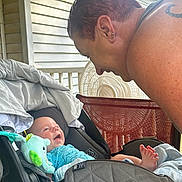 Bradley is registered to the contest to win money with this photo: baby, infant, car_seat, adult, smiling, happy, interaction, porch, fan, sunflower, tablecloth, clothing, face, person, foot, toy, blanket, earrings, tattoo, outdoor