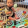 toddler, child, toy, playpen, activity_center, colorful, indoor, curly_hair, expression, playful, sitting, floor_mat, soccer_ball, infant, cute, baby, engaged, hand, clothing, headphones