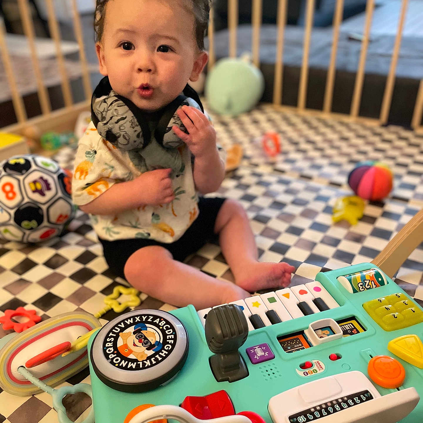 Miles joined the competition — help win amazing prizes! activity_center, baby, child, clothing, colorful, curly_hair, cute, engaged, expression, floor_mat, hand, headphones, indoor, infant, playful, playpen, sitting, soccer_ball, toddler, toy