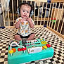 Miles is registered to the contest to win money with this photo: baby, headphones, toy_keyboard, playpen, checkered_mat, indoor, child, expression, sitting, clothing, person, face, hands, furniture, floor, cute, music_toy, colorful, young_child, home