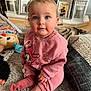 baby, child, blue_eyes, pink_clothing, topknot, sitting, rug, toy, stuffed_animal, cushion, home_interior, photograph_frames, lantern, floor, socks, cute, indoor, portrait, person, young_child
