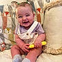 baby, child, smile, pigtails, toy, couch, blanket, pillow, socks, happy, indoor, cute, infant, seated, clothing, person, playful, home, portrait, fun
